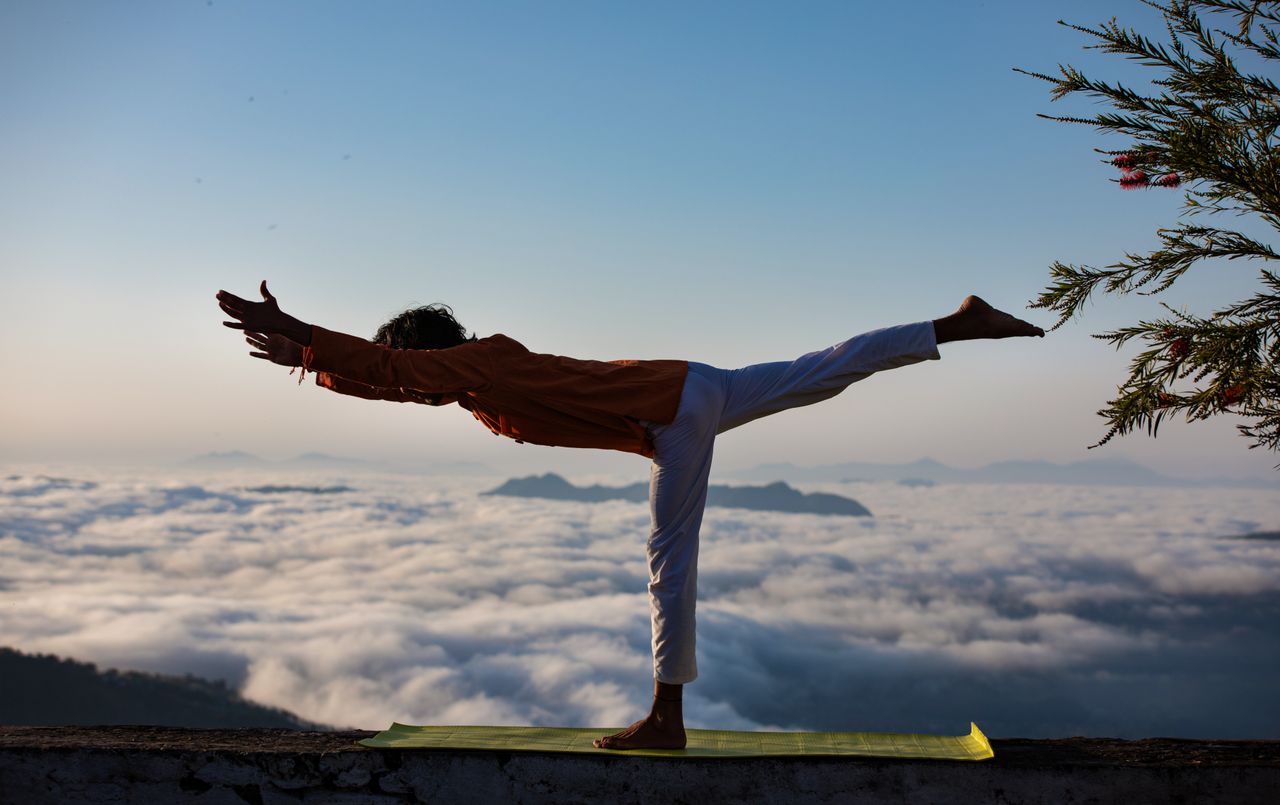 ours-journey Person practicing yoga in warrior pose above a scenic cloudscape during sunrise.